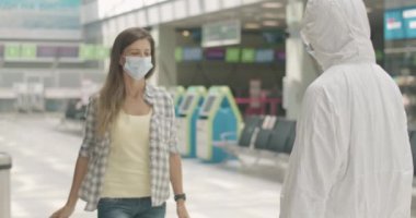 Havaalanı çalışanı, elinde esmer, beyaz maskeli bir kadın var. Covid-19 salgınının olduğu bölgeden geçen bir turist. Coronavirus turizmi. Sinema 4k ProRes Merkezi.