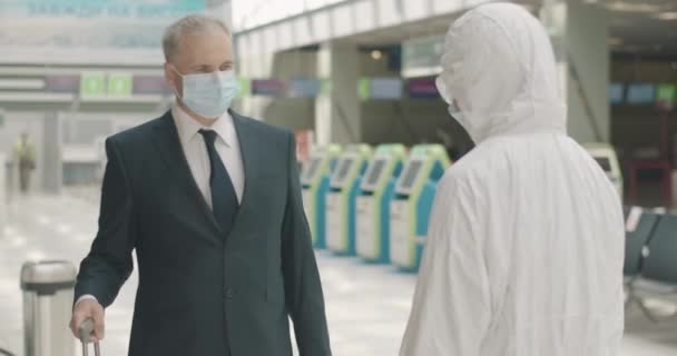 Homme d'affaires confiant masqué s'approchant d'un employé de l'aéroport qui mesure sa température et s'en va. Portrait d'un homme caucasien d'âge mûr voyageant sur une pandémie de Covid-19. Siège social Cinema 4k ProRes. — Video