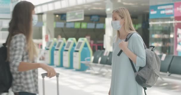 Junge Frau mit Gesichtsmaske weigerte sich Freundin zu umarmen kehrte von Reise zurück. Porträt ernsthafter kaukasischer Frauen, die sich im Ankunftsbereich des Flughafens zur Covid-19-Pandemie treffen. Coronavirus-Tourismus. Cinema 4k ProRes Hauptquartier. — Stockvideo