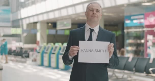 Portrait of confident handsome mid-adult man in suit standing with nameplate at arrival terminal. Elegant Caucasian guy waiting for passenger in airport. International tourism. Cinema 4k ProRes HQ. — Stock Video