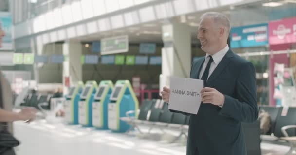 中年白人男子带着名牌在机场迎接快乐的女人。商人在等候区迎接微笑的游客.商务旅行，国际旅游。Cinema 4k ProRes HQ. — 图库视频影像