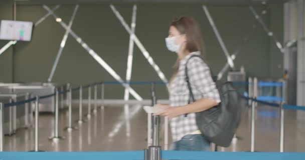 Havaalanı kapılarından geçen turistlerin sosyal mesafesini korurken yan görüntüsü. Yetişkin beyaz erkek ve kadınlar terminalde yüz maskeleriyle yürüyorlar. Covid-19 salgınında turizm. Sinema 4k ProRes Merkezi. — Stok video
