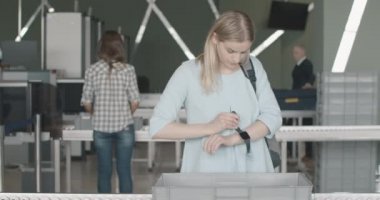 Kendine güvenen beyaz kadının portresi havaalanı terminalindeki güvenlik tepsisine kişisel eşyalarını koyuyor. Genç bayan turist kalkış bölgesinde giriş yapıyor. Sinema 4k ProRes Merkezi.