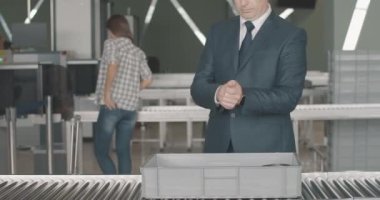 Tanımlanamayan beyaz, orta yaşlı bir adam kişisel eşyalarını güvenlik tepsisine koyuyor ve bavullarını tarayıcıya sokuyor. Kendine güvenen işadamı, kalkış terminaline giriş yapıyor. Sinema 4k ProRes Merkezi.