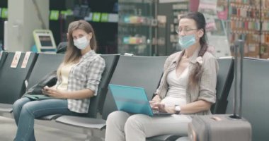 Genç ve orta yaşlı beyaz maskeli kadınlar havaalanında, otobüste ya da tren istasyonunda kalkış için bekliyorlar. Coronavirüs salgınında seyahat eden kadın turistlerin portresi. Sinema 4k ProRes Merkezi.