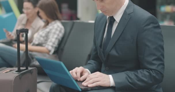Felismerhetetlen üzletember gépel laptopon a reptéri váróban. Egy magabiztos fehér férfi várja az indulást a busz- vagy vasútállomáson. Turizmus és utazás. Cinema 4k ProRes főhadiszállás. — Stock videók