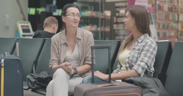 Veselé středoškolačky a mladé ženy sedící v čekárně a mluvící. Portrét šťastných turistek, které čekají na odlet na letišti, železnici nebo autobusovém nádraží. Cinema 4k ProRes HQ. — Stock video
