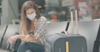 Bulanık yüzlü kadın havaalanının bekleme salonunda elinde çantasıyla akıllı telefon kullanıyor. Kadın turist Coronavirus Covid-19 salgını sırasında terminalde kalkış için bekliyor. Sinema 4k ProRes Merkezi.