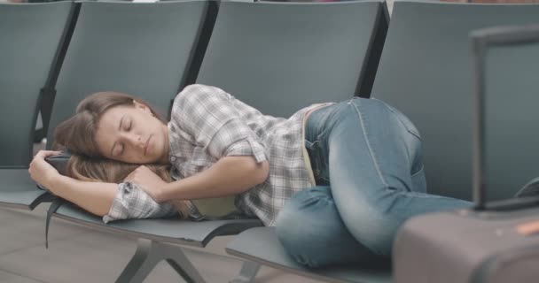 Портрет виснаженої молодої кавказької жінки, що спить на стільцях в аеропорту. Посміхнися красивою жінкою - туристкою, яка чекає відправлення на залізничну або автобусну станцію. Фільм 4k ProRes HQ. — стокове відео