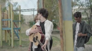 Kentteki spor sahasında yürüyen üç kendine güvenen genç adam. 1980 'lerde ya da 1990' larda gezinen ve konuşan pozitif çok ırklı arkadaşların portresi. Gitar sohbeti yapan mutlu öğrenciler. Retro biçimi.