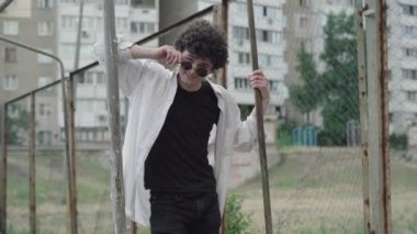 1980 'lerde ya da 1990' larda güneş gözlüğü takan ve kameraya göz kırpan beyaz bir gencin portresi. Kendine güvenen kıvırcık saçlı bir adamın şehir merkezinde flört edişinin ortası..