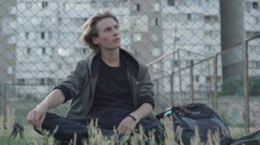 Kafkasyalı bir ergen çitte çimlerin üzerinde oturup düşünüyor. Üzgün genç adam futbol oynayan adamlara bakıyor. Dışarıda mutsuz, yalnız bir gencin portresi. Ergenlik yalnızlığı.