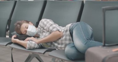 Yüzü maskeli yorgun beyaz bir kadın havaalanı, otobüs ya da tren istasyonunun bekleme salonunda koltuklarda uyuyor. Yorgun turist Covid-19 'dan kalkmayı bekliyor. Sinema 4k ProRes Merkezi.