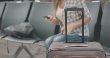 Arka planda sandalyeye uzanmış bulanık beyaz bir kadının olduğu seyahat çantasının yakın çekimi. Havaalanında ya da tren istasyonunda kalkmayı bekleyen yorgun bir bayan turist. Sinema 4k ProRes Merkezi.