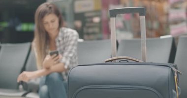 Bulanık Kafkasyalı esmer kadın önünde duran seyahat çantalı akıllı telefon kullanıyor. Genç bayan turist otobüs ya da tren istasyonunda ya da havaalanında kalkış için bekliyor. Sinema 4k ProRes Merkezi.