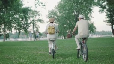 Parkta bisiklete binen pozitif orta yaşlı bir çiftin geçmişe bakışı. Açık havada güneşli bir günün tadını çıkaran aktif, neşeli beyaz erkek ve kadın. Mutlu aile birlikte eğleniyor..