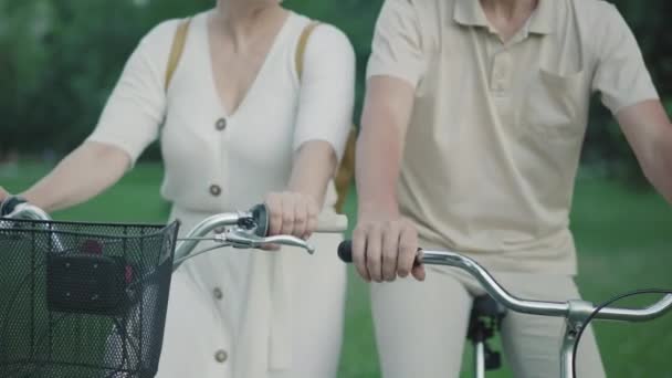 Αγνώριστο ενήλικο ζευγάρι που κάθεται σε ποδήλατα στην ύπαιθρο. Σύζυγος να παίρνει το χέρι του συζύγου, σύζυγος να βάζει το κεφάλι στον ώμο του. Λατρεύει την ενεργή λευκή οικογένεια που ξεκουράζεται στο πάρκο. Ενότητα, αγάπη, ψυχαγωγία. — Αρχείο Βίντεο