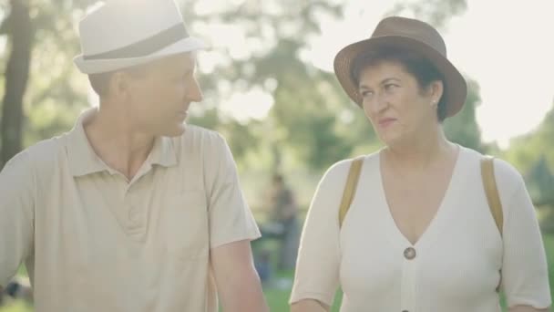 Средний снимок улыбающихся мужчин и женщин, флиртующих в солнечных лучах в парке. Портрет позитивной пожилой белой пары на романтическом свидании на закате. Вечная любовь, связь, счастье. — стоковое видео