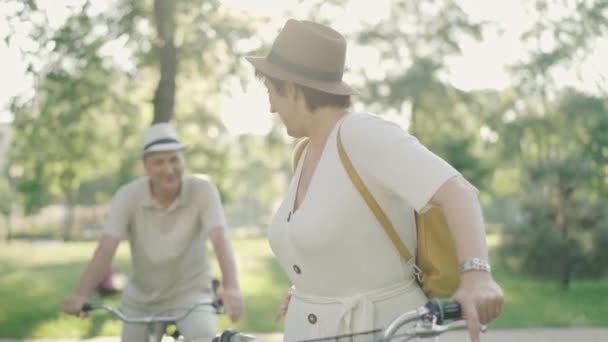优雅的中年白人女人在背后对着微笑模糊的男人说话，转过头去对着相机微笑。夏至公园里骑自行车与丈夫调情的积极妻子的画像. — 图库视频影像