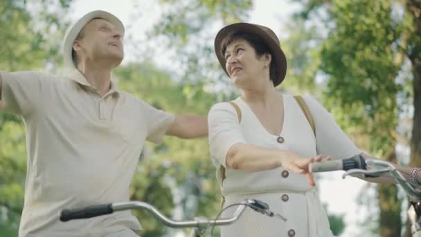 Homem e mulher felizes com as mãos esticadas desfrutando da luz solar no parque de verão. Retrato de casal caucasiano feliz positivo em bicicletas se divertindo no dia ensolarado ao ar livre. Estilo de vida ativo, felicidade . — Vídeo de Stock