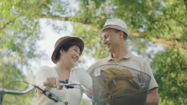 在阳光明媚的公园里拥抱和聊天的中年夫妇的画像。积极的白人丈夫和妻子享受日落户外骑自行车。夏日快乐的家人聊天，欢笑. — 图库视频影像