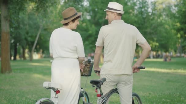 Vue arrière du couple aimant se regardant et s'embrassant. Heureux mi-adulte Caucasien homme et femme avec des vélos passer du temps ensemble à l'extérieur dans un parc d'été ensoleillé. — Video