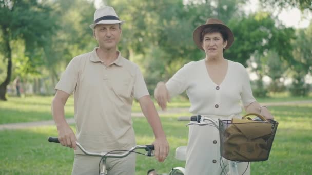 Портрет радостного мужчины и женщины, снимающих шляпы и улыбающихся в камеру. Позитивная белая пара позирует в летнем парке на закате. Счастливые любящие муж и жена встречаются на открытом воздухе в солнечный день. — стоковое видео