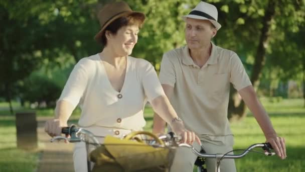 Alegre hombre y mujer caucásicos sentados en bicicletas y decidiendo en el camino. Retrato de una sonriente pareja adulta de pie a la luz del sol al atardecer. Feliz marido y mujer citas al aire libre. — Vídeos de Stock