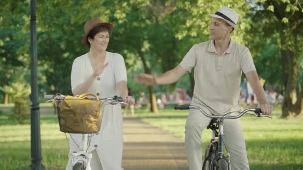 Retrato de casal médio-adulto confiante positivo dando alta cinco e sorrindo para a câmera. Marido e esposa caucasianos felizes desfrutando de passeio de bicicleta ao pôr do sol no parque de verão. Nitidez, alegria . — Vídeo de Stock