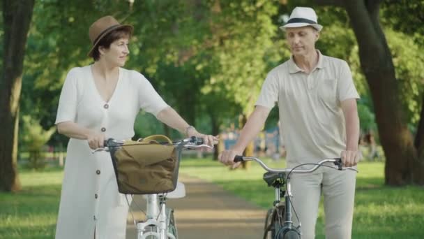 Pozytywnie kochający mężczyzna i kobieta, chodzący z rowerami i mówiący. Portret kaukaskiego męża i żony datowanych na zachód słońca w letnim parku. Szczęśliwa para odpoczywa na świeżym powietrzu w weekendy. — Wideo stockowe