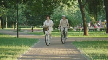 Gün batımında yaz parkında bisiklet süren neşeli orta yaşlı kadın ve erkek. Dışarıda bisiklet sürmekten hoşlanan mutlu beyaz bir çiftin portresi. Aile eğleniyor. Boş zaman, yaşam tarzı..
