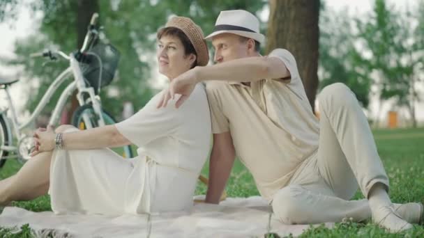 Elegancka para rasy białej, siedząca na kocu w letnim parku i gawędząca. Portret szczęśliwego pozytywnego mężczyzny i kobiety cieszących się zachodem słońca na zewnątrz. Data radosnej kochającej rodziny. — Wideo stockowe