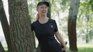 Yaz parkında ısınan bir orta yaşlı sporcunun portresi. Güneşli bir günde, bacakları esneyen gülümseyen beyaz kadın. Aktif bayan açık havada temiz hava eğitimi alıyor. Fitness konsepti.