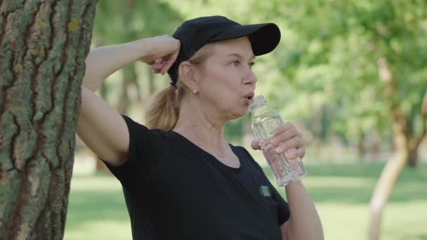 Side view boldog középkorú sportolók ivóvíz edzés után a nyári parkban. Portré elégedett vékony középkorú kaukázusi nő pihenő edzés után szabadban. — Stock videók