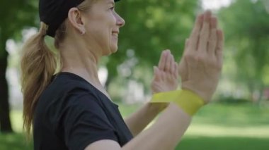 Kendine güvenen neşeli sporcu bayanın dışarıda direniş bandıyla egzersiz yaptığı yakın plan görüntüsü. Güneşli yaz parkında beyaz, orta yaşlı kadın eğitimi. Spor egzersizi..