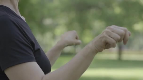 Mujer caucásica irreconocible de mediana edad calentando las manos en el parque de verano. Deportiva segura haciendo ejercicio al aire libre en un día soleado. Estilo de vida activo, deporte, fitness. — Vídeos de Stock