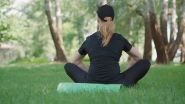 Egzersiz minderinde oturan ve nefes alan orta yaşlı bir sporcunun arka planı. Güneşli bir sabahta açık havada çalışan Kafkas Yogi kadın. Sarışın kadın yaz parkında antrenman yapıyor..
