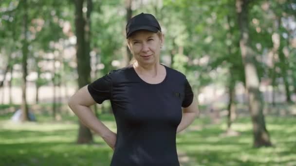 Portret van een zelfverzekerde, volwassen vrouw die haar middel buiten meet. Slanke mooie blanke sportvrouw met meetlint in zonnig zomerpark. Trainen en gewichtsverlies. — Stockvideo