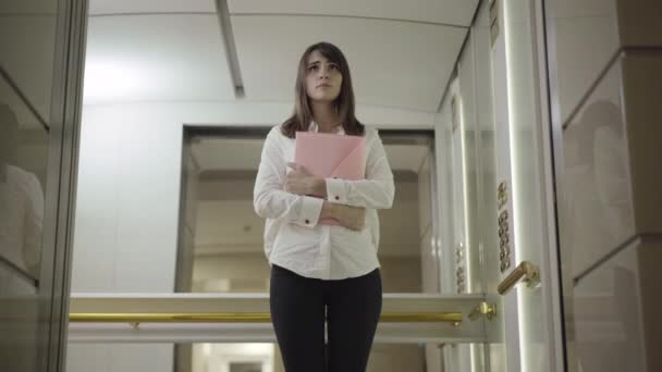 Αγχωμένη νεαρή επιχειρηματίας στέκεται στο ασανσέρ με έγγραφα και πόρτα ασανσέρ κλείνει. Πορτρέτο της αμήχανης όμορφης καυκάσιας γυναίκας με κομψό ντύσιμο που εργάζεται στο επιχειρηματικό κέντρο. Επιχειρηματική έννοια. — Αρχείο Βίντεο