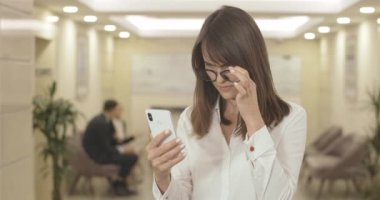 Gözlüklü, akıllı telefon ekranında okumaya çalışan kafası karışmış esmer kadının portresi. Güzel beyaz iş kadını çok çalıştığı için görme sorunu yaşıyor. Sinema 4k ProRes Merkezi.