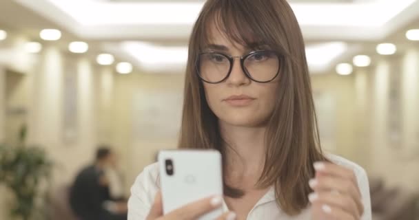 Närbild av vackra brunett affärskvinna med bruna ögon läser på smartphone. Porträtt av överarbetad vit kvinna i glasögon med synproblem. Bio 4k ProRes HQ. — Stockvideo