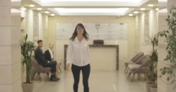 หญิงสาวที่มั่นใจ เดินไปตามหอประชุมศูนย์ธุรกิจ ข้ามมือและยิ้มที่กล้อง รูปภาพของนักธุรกิจหญิงผิวขาวที่ประสบความสําเร็จในแว่นตาที่โพสในสํานักงาน โรงภาพยนตร์ 4k ProRes HQ . — วีดีโอสต็อก