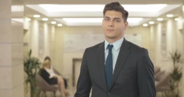 Zarif takım elbiseli, saçları düzelten ve kameraya gülümseyen yakışıklı, kendine güvenen beyaz adamın portresi. İş merkezinde poz veren başarılı bir iş adamı. Sinema 4k ProRes Merkezi..