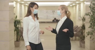 İş merkezinde el sıkışmak yerine dirseklerine dokunan maskeli iki iş kadını. Covid-19 salgınında iş anlaşması yapan Kafkas kadınlarının portresi. Sinema 4k ProRes Merkezi.