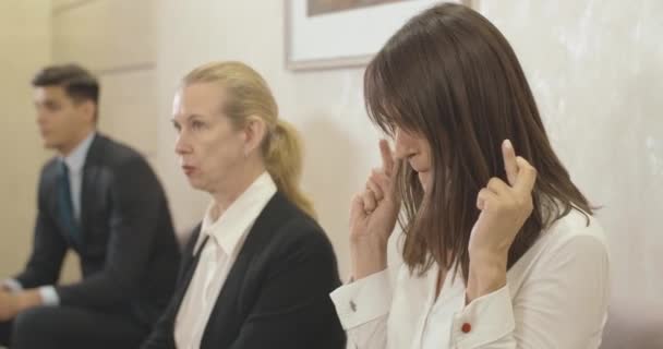 Jeune femme caucasienne stressée croisant les doigts avant l'entrevue d'emploi. Nerveux belle candidate qui attend avec d'autres hommes d'affaires dans le hall du bureau. Siège social Cinema 4k ProRes. — Video