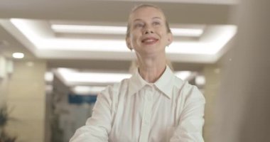 Kendine güvenen orta yaşlı bir kadın iş merkezinde resepsiyona yaklaşıyor ve gülümsüyor. Sarışın Kafkas iş kadını ofisinde toplantı programını netleştirdi. Sinema 4k ProRes Merkezi.