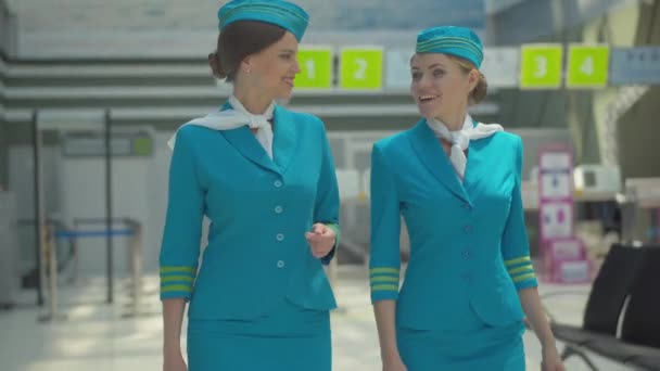 两个自信漂亮的空姐在机场散步聊天。迷人的笑容满面的白人女性形象,穿着蓝色空服员制服聊天.国际旅游概念. — 图库视频影像