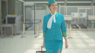 Havalimanında seyahat çantasıyla yürüyen güzel bir hostes. Uçuş görevlisi üniformalı, kendine güveni tam beyaz bir kadının portresi kalkışa hazırlanıyor ya da seyahatten sonra eve geliyor..