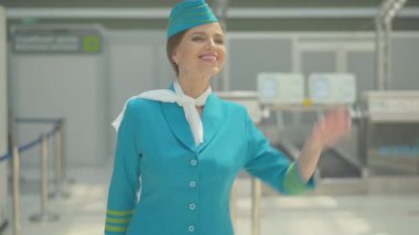 Çekici yetişkin hostesin gülümseyerek el salladığı ve seyahat çantasıyla ayrıldığı portresi. Geldikten sonra üniformalı güzel, beyaz bir kadın. Yurt dışına seyahat eden uçuş görevlisi..