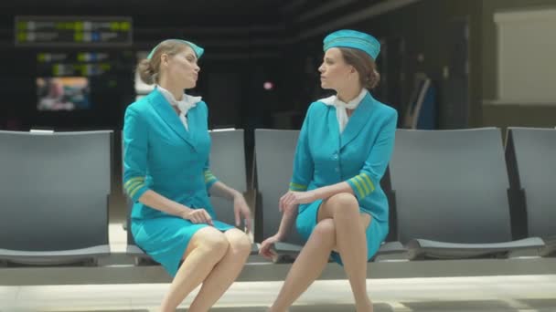 Porträtt av ung flygvärdinna som klagar över nacksmärtor till kollegan. Smala vackra vita kvinnor i uniform diskuterar yrkessjukdomar i flygplatsterminalen före avgång. Yrkesproblem. — Stockvideo